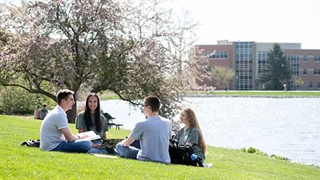 四个学生坐在湖边的草地上读书